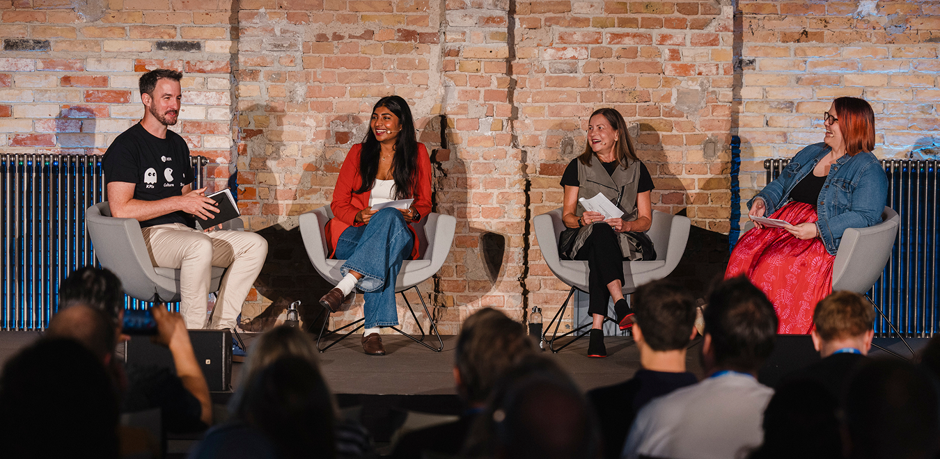 Vier Personen in einer Panel-Diskussion auf der Bühne, sitzend in Sesseln vor einer Backsteinwand.