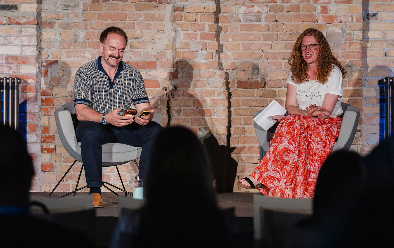 Fireside Chat auf der Bühne: Ein Mann und eine Frau sitzen einander gegenüber und lachen.