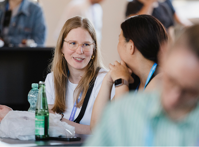 Zwei Personen im Gespräch bei einer Networking-Session, im Vordergrund eine junge Frau mit Brille, die lächelnd zuhört.